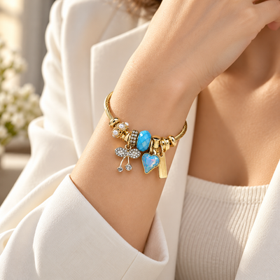 Woman wearing ANOVRA gold-tone blue charm bracelet with heart and crystal charms, face not visible.