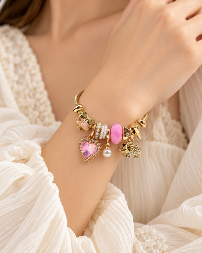 Close-up of ANOVRA gold-tone charm bracelet featuring pink gemstone-style beads, sparkling heart pendant, pearls and elephant charm.