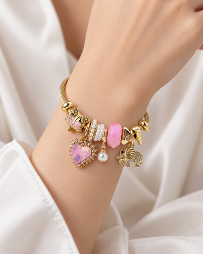 ANOVRA pink charm bracelet styled on a model's wrist, featuring gold-tone detailing, pink crystal heart and elephant charms.