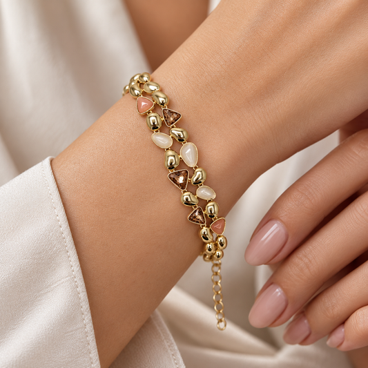 Close-up of gold-tone bracelet with blush pink, white and champagne-toned decorative accents