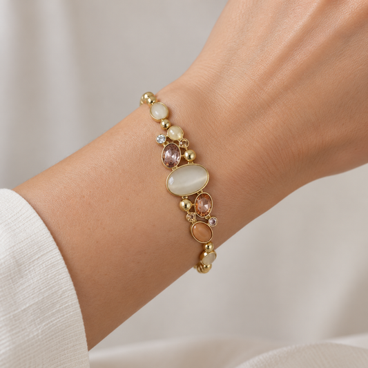 Close-up of ANOVRA Pastel Aura gold tone statement bracelet on wrist, highlighting oval ivory and peach stones with delicate crystal embellishments.