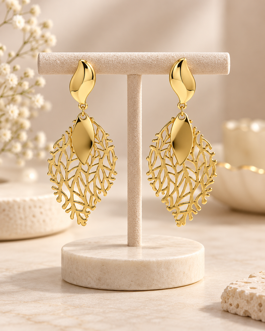 ANOVRA golden leaf statement earrings styled with minimal luxury props on a cream background.