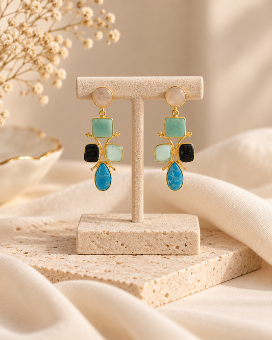 ANOVRA multicolour stone drop earrings styled with minimal luxury props against a soft cream background.