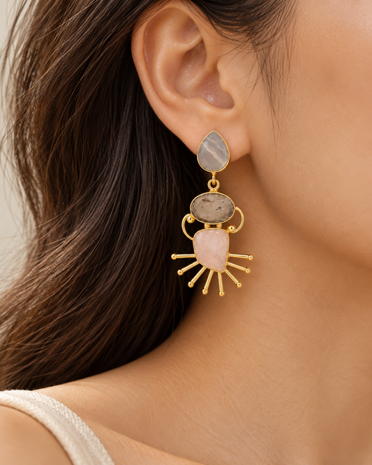 Close-up of statement earrings featuring teardrop and oval stones with intricate gold sunburst accents.