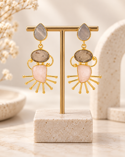 ANOVRA multicolour gemstone-style statement earrings displayed with minimal luxury props on a cream background.