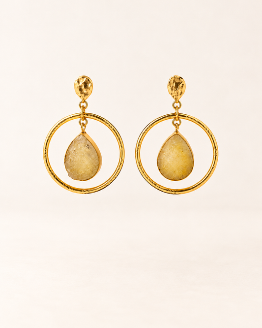 ANOVRA gold teardrop hoop earrings featuring textured circular frames and golden-yellow dangling stone accents.